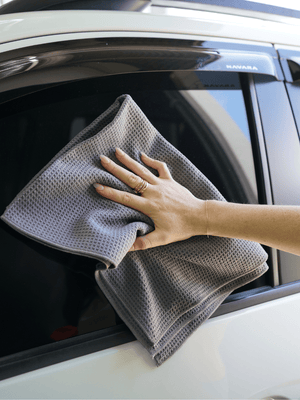 Person cleaning a car window with a gray microfiber cloth