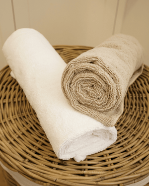 Two rolled towels, one white and one beige, on a wicker basket.