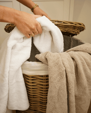 Person holding white towels next to a wicker laundry basket with brown towel.
