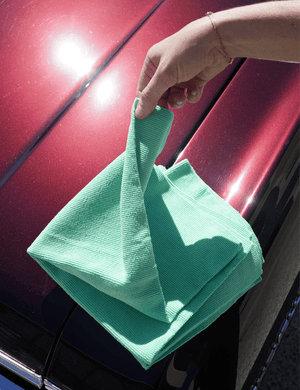 A person holding a green microfibre pearl knit cloth on top of a red car