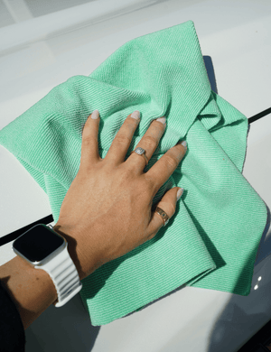A person holding a green microfibre cloth on a white car